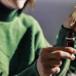 En esta fotografía aparece una mujer de saco verde sosteniendo con sus manos un tarro de aceite. Esta imagen se utiliza para complementar un blog sobre por que una persona debería utilizar cbd.