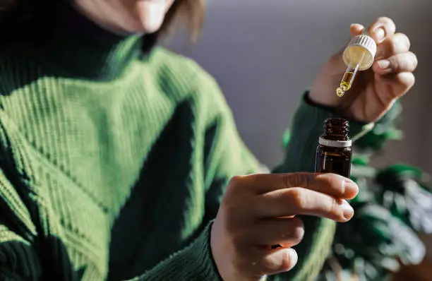 En esta fotografía aparece una mujer de saco verde sosteniendo con sus manos un tarro de aceite. Esta imagen se utiliza para complementar un blog sobre por que una persona debería utilizar cbd.