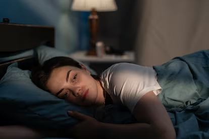 En la fotografía se muestra una mujer con el rostro cansado recostada en su cama. Esta imagen se utiliza para complementar un blog sobre insomnio e hipersomnia