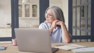 En la fotografía aparece una mujer con la mirada perdida hacia un costado frente a su computador. Esta imagen se utiliza como portada para un blog sobre como elegir el producto de cbd adecuado para cada persona.